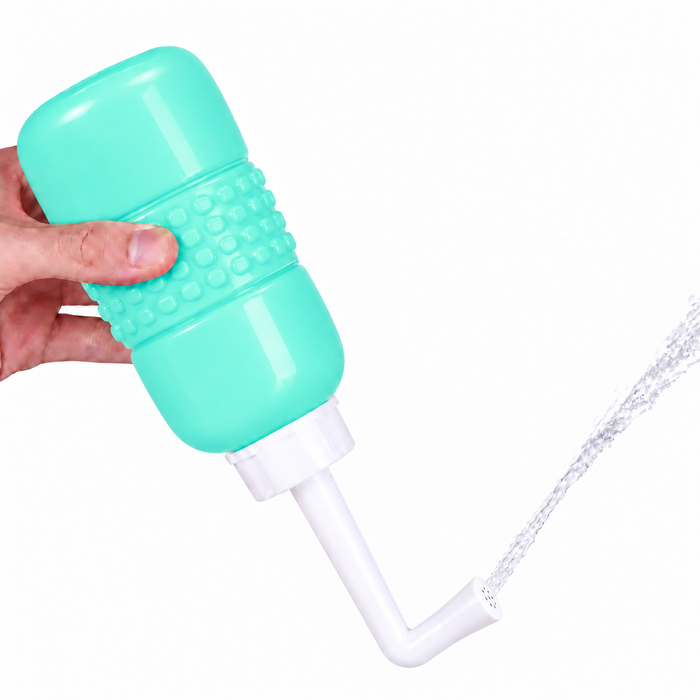A hand holding a mint green squeeze peri or bidet postpartum bottle with a white spout that is spraying water, shown against a plain white background.